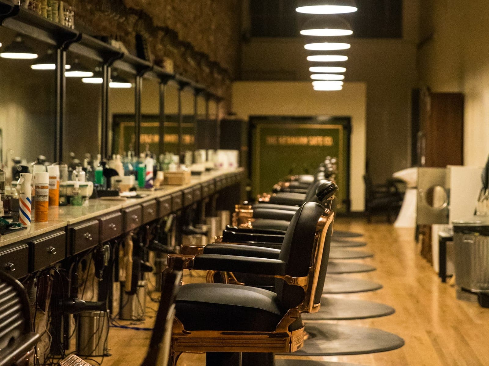 A row of leather barber chairs along a mirrored wall under pendant lamps